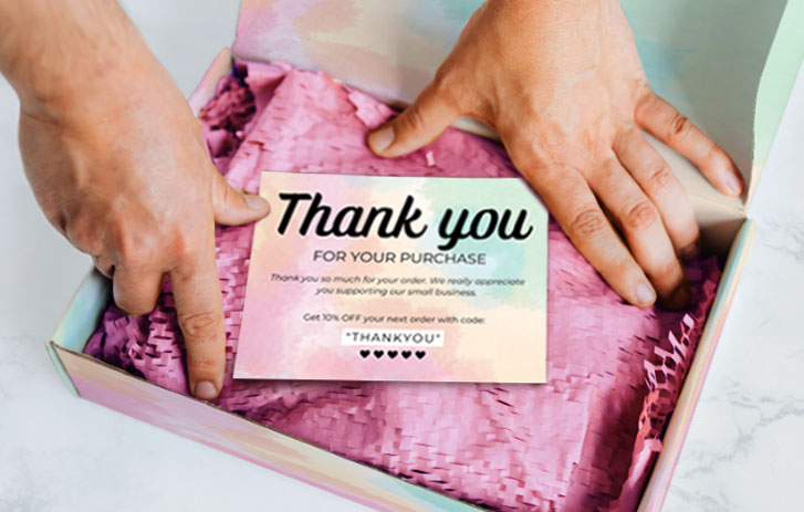 A person packing a box with a printed thank you card on top